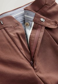 Brown trousers feature a zip fly, button closure, and a contrasting light blue waistband. The material is smooth and slightly textured.