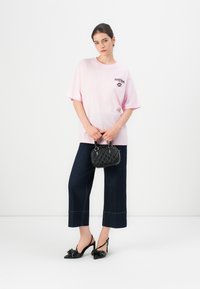 Ružové nadmerné tričko s grafickou potlačou, tmavé deninové culotte nohavice, čierna štruktúrovaná kabelka a čierne slingback sandále so detailom mašle.
