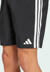 Crne sportske kratke hlače s bijelim prugama sa strane i bijelim trokutastim logotipom na donjoj lijevoj strani. Lagani, glatki materijal.