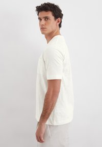 Kurzarm, off-white Hemd aus leichtem Stoff, mit einer Brusttasche und einem lässigen Schnitt. Glatte Textur mit subtiler Farbvariation.