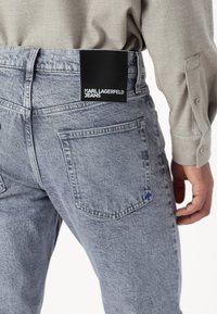 Vaqueros de mezclilla azul claro con un acabado texturizado, que presentan una etiqueta de cuero negra que dice "KARL LAGERFELD JEANS" en la cinturilla.