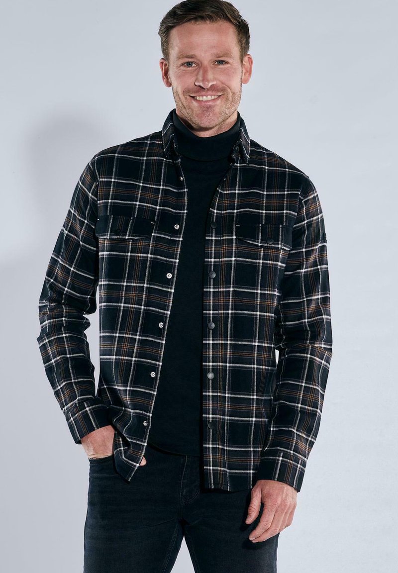 Schwarz-weiß kariertes Hemd mit orangefarbenen Akzenten, Knopfleiste, zwei Brusttaschen und langen Ärmeln, getragen über einem schwarzen Rollkragenpullover.