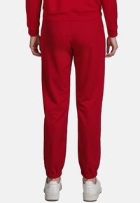 Rode joggingbroek met elastische boorden en tailleband, gemaakt van zachte stof. Draagt met witte sneakers, wat zorgt voor een ontspannen pasvorm.