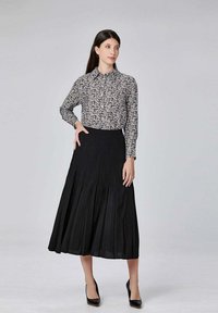 Jupe plissée noire associée à une chemise à manches longues à motifs floraux blancs et noirs. Mannequin portant des talons hauts noirs ; arrière-plan neutre.