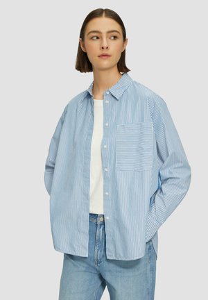 Chemise boutonnée rayée bleu clair avec une poche poitrine, coupe décontractée, manches longues et une couche intérieure blanche visible en dessous.