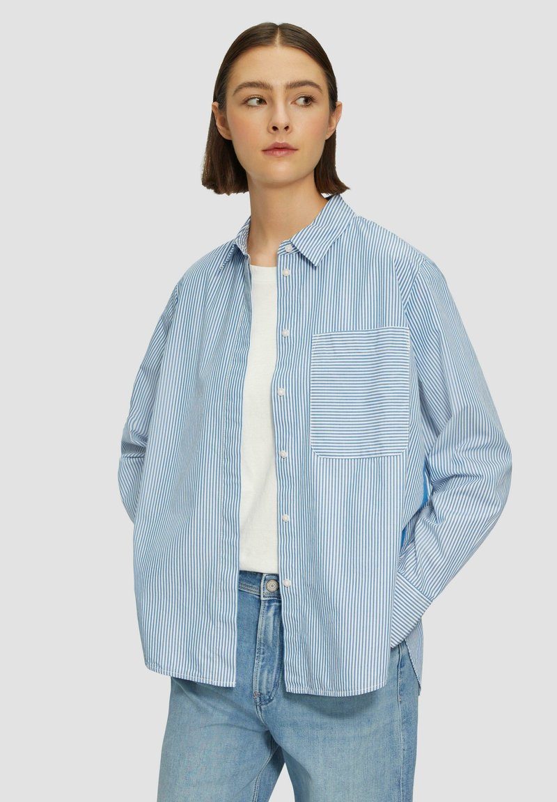 Chemise boutonnée rayée bleu clair avec une poche poitrine, coupe décontractée, manches longues et une couche intérieure blanche visible en dessous.