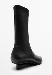 Stivale alla caviglia in pelle nera con una superficie liscia, forma affusolata e tacco a zeppa. Presenta una tomaia senza cuciture e un design minimalista.