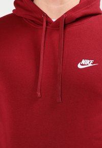 Czerwona bawełniana bluza z kapturem z przodu, z kieszenią typu kangur, regulowanymi sznurkami i białym logo Nike na klatce piersiowej.