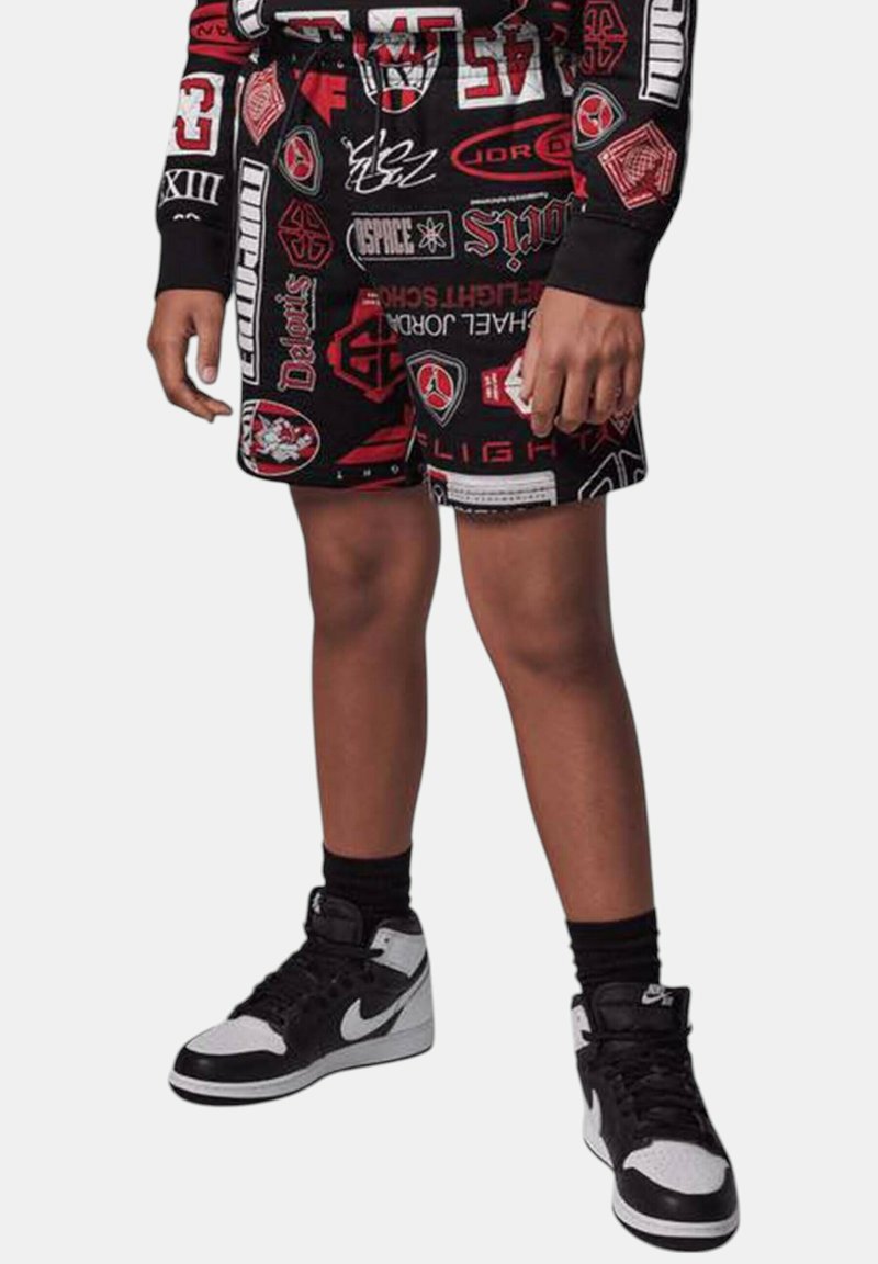 Pantaloni corti neri con vari loghi audaci rossi e bianchi; abbinati a sneakers alte nere e bianche e calze nere.