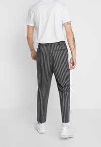 Kevyt, harmaa housut valkoisilla raidoilla, joissa on joustava vyötärönauha, kapeneva leikkaus ja yksi takatasku. Yhdistetty valkoiseen T-paitaan.