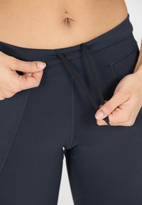 Höga mörkblå träningsleggings med flat midja och yttre dragsko. Slät tyg med dekorativa sömmar.