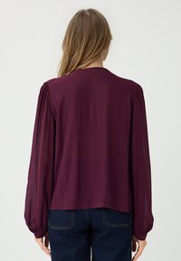 Blusa bordeaux con maniche lunghe e vaporose e scollatura rotonda. Realizzata in tessuto leggero con una texture liscia e una vestibilità rilassata.