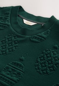 Ciemnozielony sweter z teksturowanymi, wypukłymi ozdobami świątecznymi i wzorami. Prążkowany dekolt i tkanina o miękkim wykończeniu.