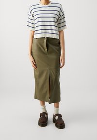 Randig kortärmad tröja i kräm och marin, olivgrön pennkjol med slits fram, bruna träskor med remmar och ljusa strumpor.