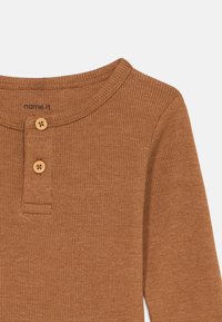 Camisa castanha de manga longa com gola redonda, apresentando dois botões de madeira na frente e detalhes de costura subtil.