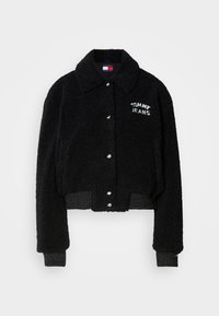Veste courte noire en matière pelucheuse, dotée d'une fermeture à boutons, d'un col et d'une broderie blanche "TOMMY JEANS" sur la poitrine.