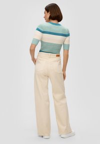 Strickoberteil mit kurzen Ärmeln in Petrol- und Cremestreifen, kombiniert mit weiten cremefarbenen Hosen. Sichtbare Gesäßtaschen und ein Lederlabel an der Taille.