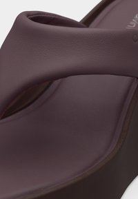 Κοντινή λήψη ενός σκούρου μοβ πέδιλου με φαρδιά μαξιλαρωτή λουρίδα και σόλα πλατφόρμας, που αναδεικνύει την ομαλή υφή δέρματος και τον καμπυλωτό σχεδιασμό.