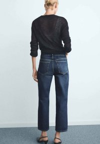 Pull en maille noir, jean droit taille haute bleu foncé, vue arrière, avec deux poches arrière et un détail de couture minimal.