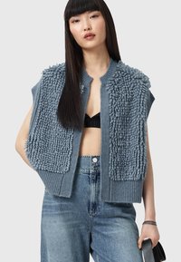 Gilet lavorato a maglia di colore azzurro chiaro con una superficie morbida, apertura frontale e orlo a coste. Abbinato a jeans in denim a vita alta.