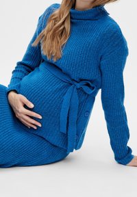Ensemble pull côtelé bleu et jupe assortie, doté d'une taille à nouer, d'un tissu texturé et de boutons décoratifs sur le côté.