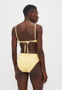 Gul ribbet bikinisett med justerbare stropper og knytedetalj på baksiden; høy midje-bunn med glatt tekstur og minimale sømmer.