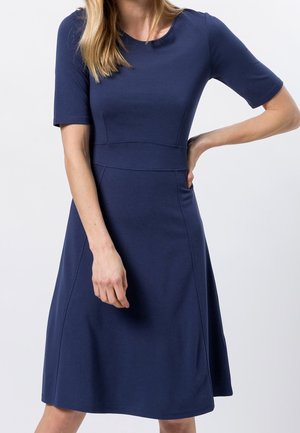 Marineblå kjole med korte ærmer, tætsiddende overdel og udflared skørt. Glat, elastisk stof med rund halsudskæring og sømdetaljer.