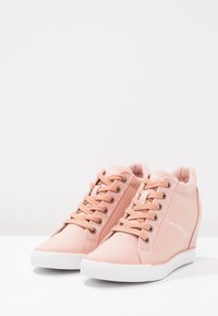 Světle růžové plátěné tenisky s nízkým profilem, kulatou špičkou, gumovou podrážkou a logem na boku. Mají šněrování vpředu a dekorativní švy.