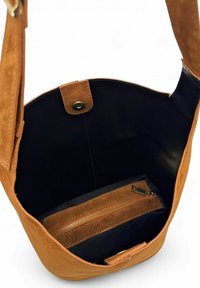 Sac bandoulière en daim marron avec un intérieur noir, comprenant une poche zippée et un fermoir à pression magnétique. Texture lisse et design épuré.