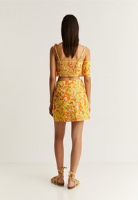 Heldergele twee-delige outfit met een gesmokte crop top met off-shoulder mouwen en een bijpassende mini rok met bloemmotieven.