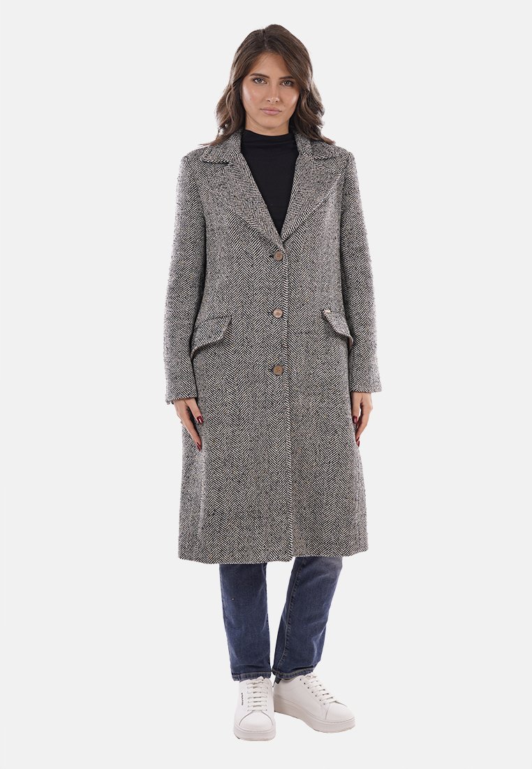 Cappotto in lana a spina di pesce grigio con due tasche frontali e bottoni. Maniche lunghe e colletto classico, abbinato a jeans blu e sneakers bianche.