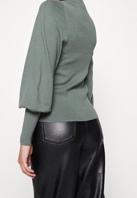 Zielony dzianinowy sweter z bufiastymi rękawami i dopasowaną talią, zestawiony z wysokim stanem czarnych skórzanych spodni z naszywanymi kieszeniami.