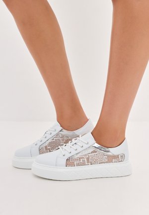 Zapatillas blancas con acentos beige texturizados y detalles en plata. Presentan cordones y una suela gruesa blanca.