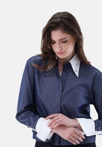 Navy blue blouse with a white collar and cuffs, featuring button closure and fine stitching details. Soft fabric with a structured fit.