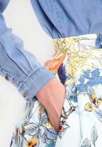 Jeansskjorta med långa ärmar och knappade manschetter, kombinerad med en blomstermönstrad kjol i blå, gula och orange nyanser. Kjolen har sidfickor.