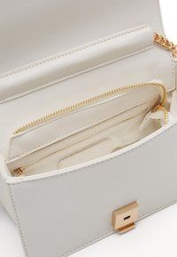 White leather handbag featuring a gold-tone clasp, interior zipper pockets, and a smooth texture. Compact design with minimalist accents.