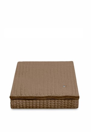 Opgevouwen bruine deken met wafelstructuur en een klein rond zilverkleurig label op een witte achtergrond.