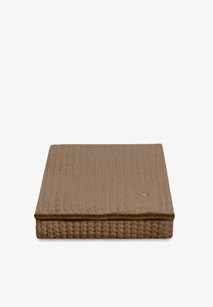 Opgevouwen bruine deken met wafelstructuur en een klein rond zilverkleurig label op een witte achtergrond.