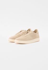 Scarpe da ginnastica beige realizzate in tessuto a rete, con una superficie texturizzata, lacci piatti e suola in gomma resistente dal design semplice.