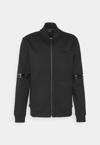 Veste noire à fermeture éclair avec col haut, deux bandes brillantes sur chaque manche, poches avant et logo "BOSS" sur la poitrine gauche.