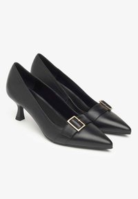 Black leather high-heeled shoes with a pointed toe and a small gold buckle accent on the strap. Textured material and sleek design.
