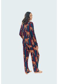 Conjunto de pijama de manga larga en rayas rojo oscuro y verde azulado, con grandes patrones de tigre naranja. Tela suave y corte relajado, con pantalones a juego.