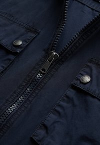 Dark navy jacket with a smooth texture, featuring a central zipper, metal snaps, and flap pockets. Stitching is visible along the seams.