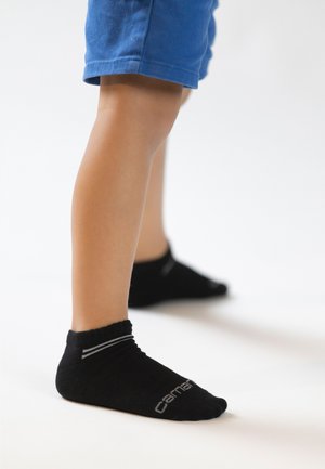 Schwarze Knöchelsocken mit Ribbenbündchen und zwei grauen Streifen, kombiniert mit blauen Shorts. Der Hintergrund ist schlicht weiß.