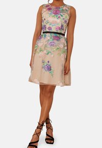 Bezramínková béžová šaty s květinovou výšivkou v purpurové a zelené barvě, stažený pas, průhledná vrstva a černý pás. Černé sandály na vysokém podpatku s pásky.