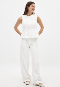 Biely peplum top vyrobený z textúrovanej látky, kombinovaný so širokými nohavicami. Obe sú v jednofarebnej bielej farbe, majú voľný a uvoľnený strih.