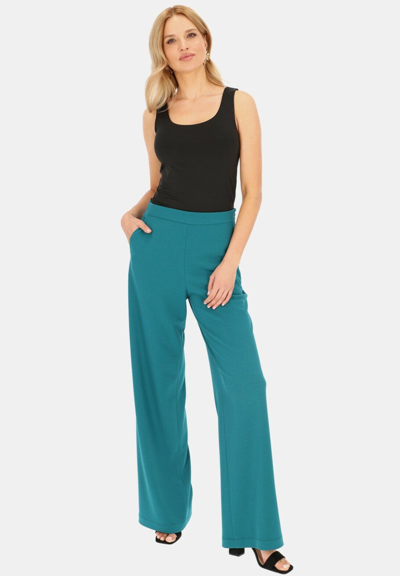 Miękkie, turkusowe spodnie o szerokich nogawkach, z wysokim stanem i bocznymi kieszeniami, w połączeniu z czarnym bezrękawnikiem. Elegancki, luźny krój.