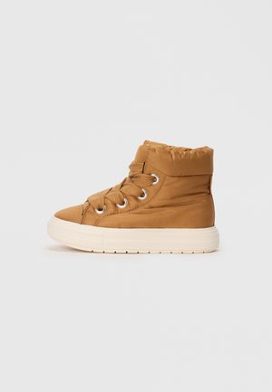Kohvatanane kõrgel välimusel sneaker, millel on polsterdatud krae, tekstureeritud paelad, ümar varvas ja heledat värvi tallad. Omab metallist silmuseid paelte jaoks.