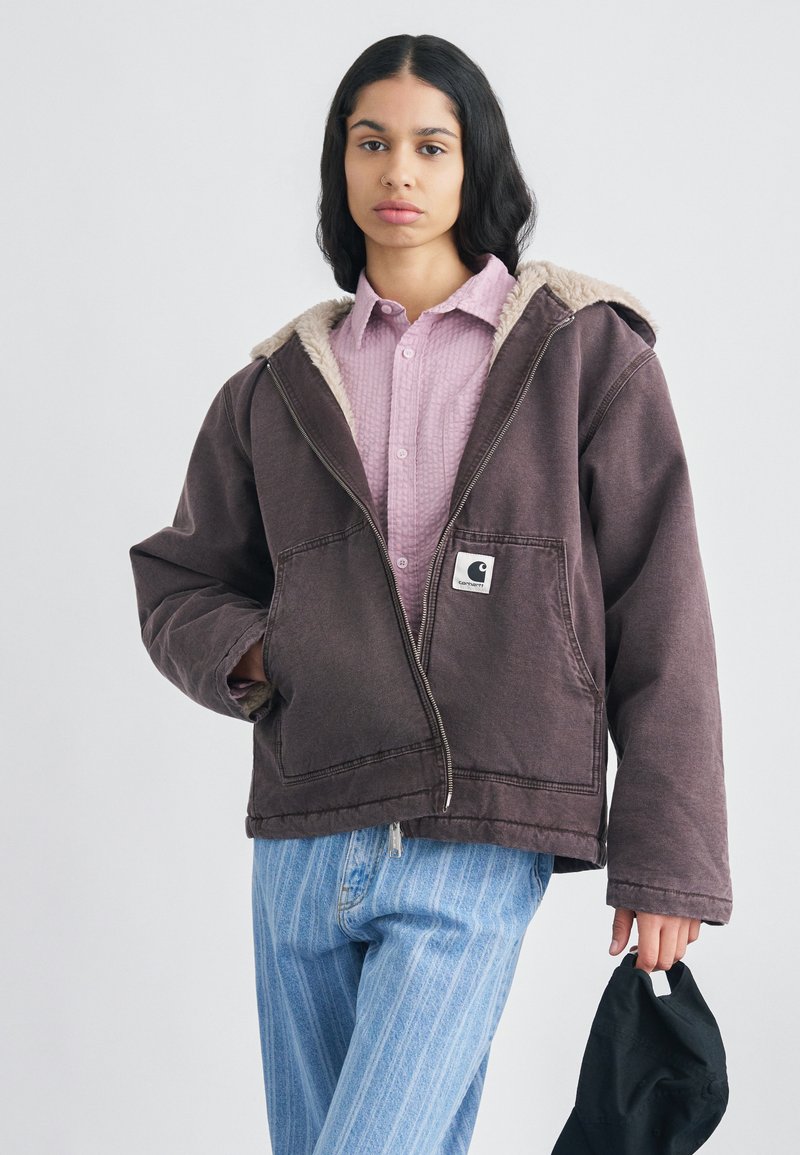 Barna kapucnis pulóver krémszínű béléses kapucnival, két első zsebbel és logófolttal. Világos kockás inggel és csíkos farmerral párosítva.