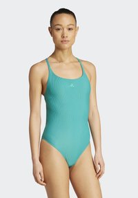 Tyrkysový jednodílný plavky s jemným texturováním, tenkými ramínky a nenápadným logem na hrudi. Navržené s vysokým vykrojením nohavic.
